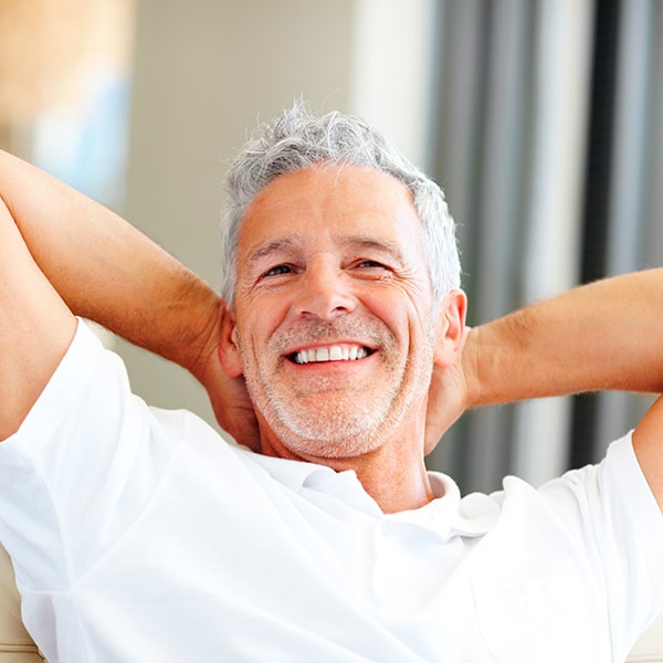 A man is smiling with teeth while placing his hands on the back of his neck