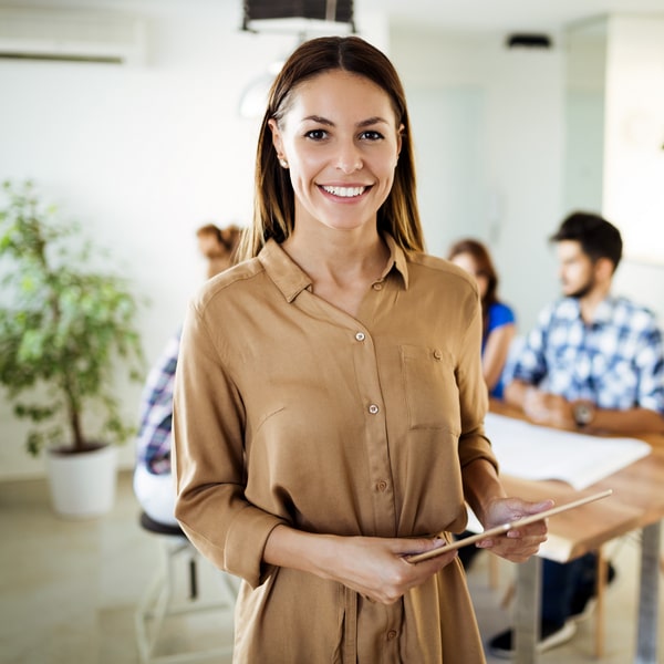 A woman in a dress is happily smiling while holding her Ipad