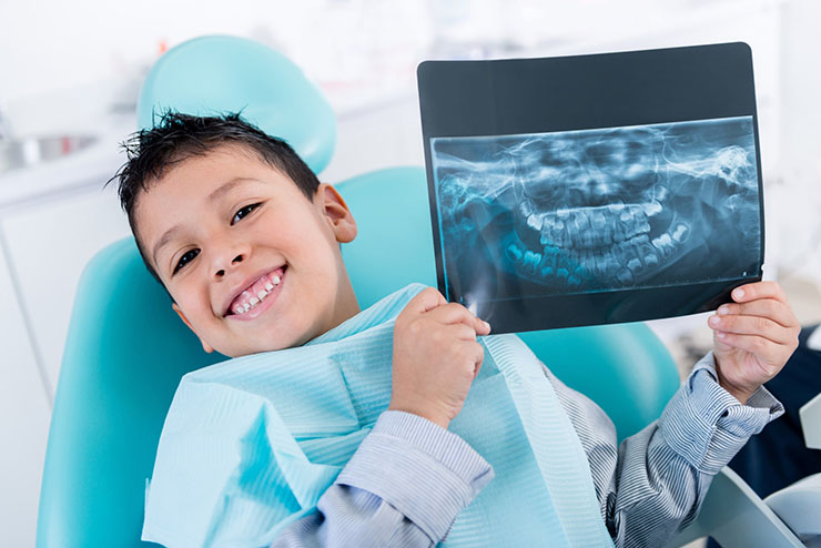 Young boy smiles and holds up his dental X-rays